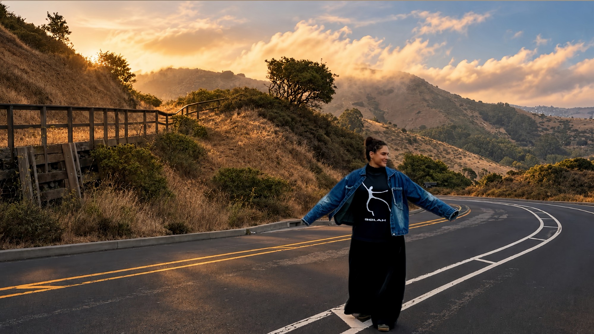 Polina on a winding coastal road at sunset, arms out